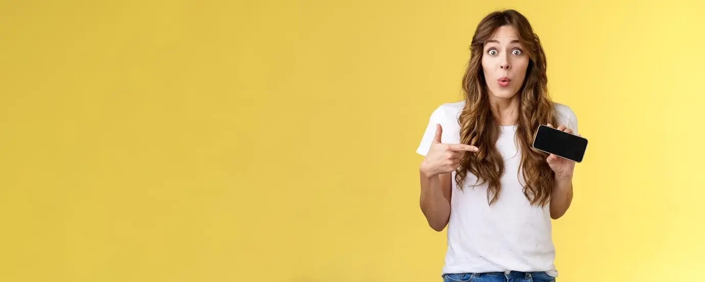 Удивлённая, восторженная, заинтригованная милая кудрявая девушка европейской внешности, складывающая губы, забавляясь и проявляя любопытство.